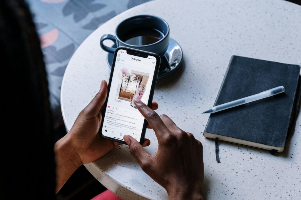 A user scrolling through Instagram on their phone, with coffee and a notebook on the table.