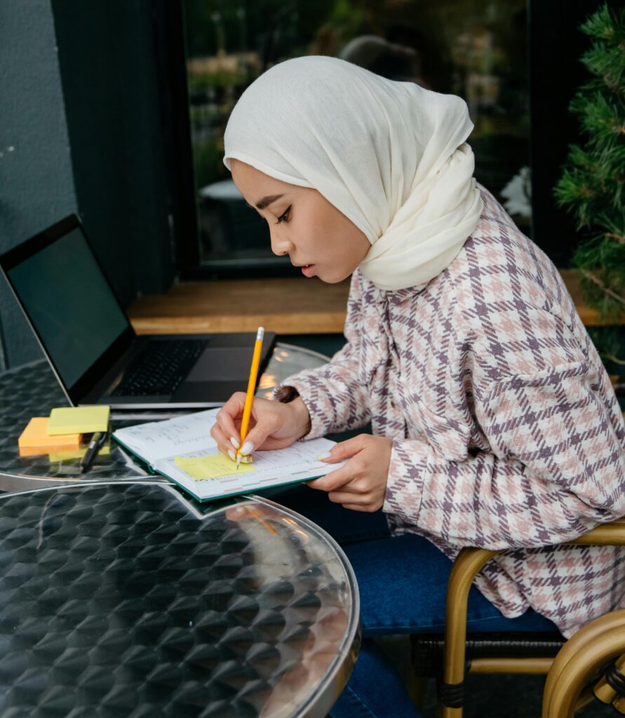A student in a hijab annotating her reading from her laptop.